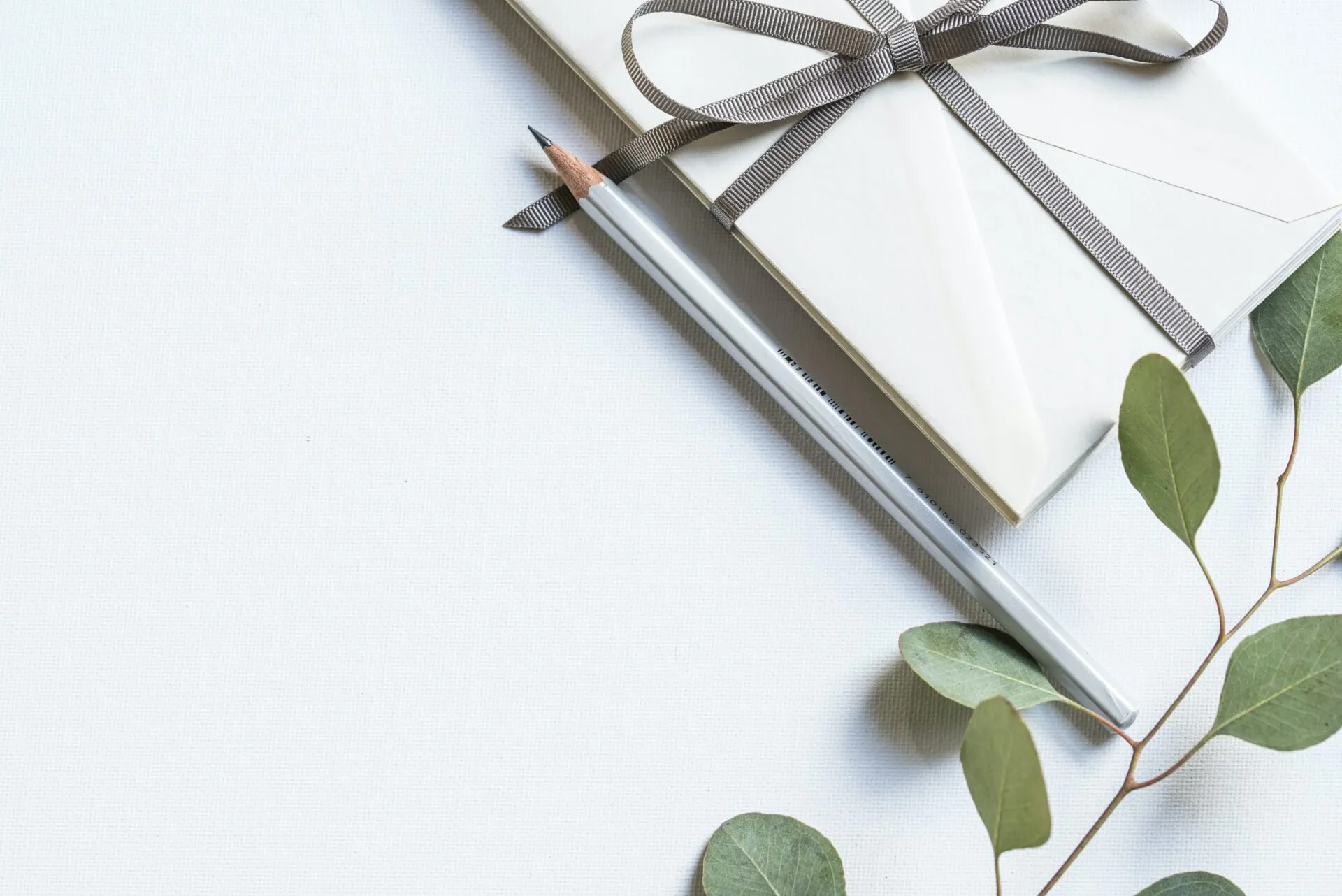 Weiß verpacktes Geschenk mit Schleife, Bleistift und Eukalyptuszweig