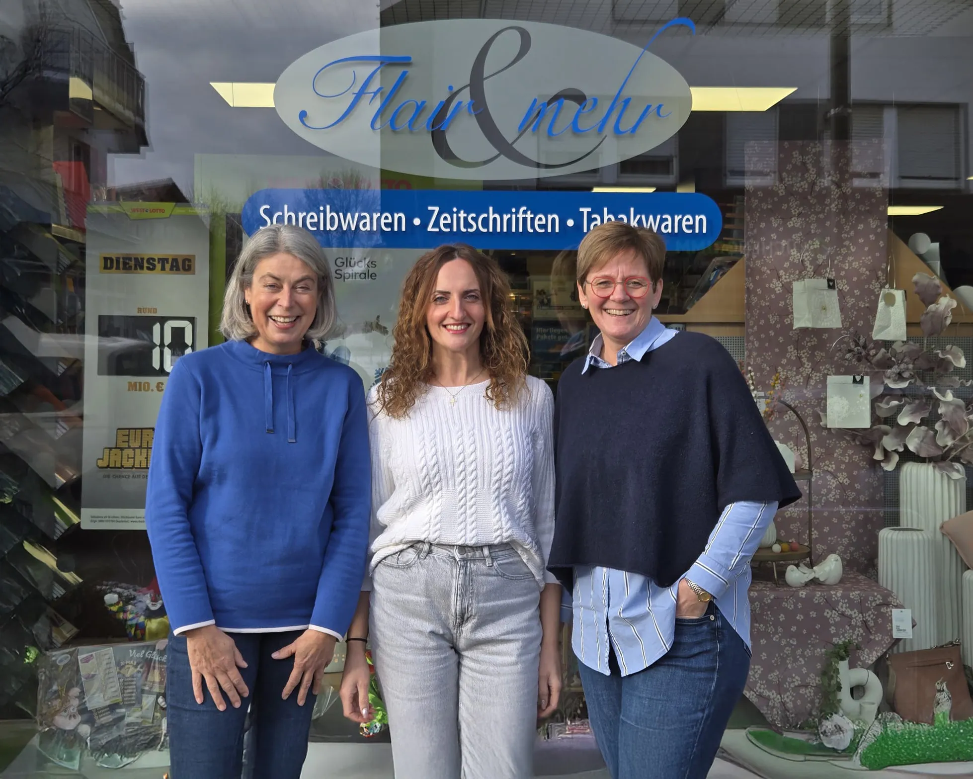 Drei Mitarbeiterinnen von Flair & mehr vor dem Schaufenster des Ladens, daneben Plakate von WestLotto und ein Schild mit Schreibwaren, Zeitschriften und Tabakwaren