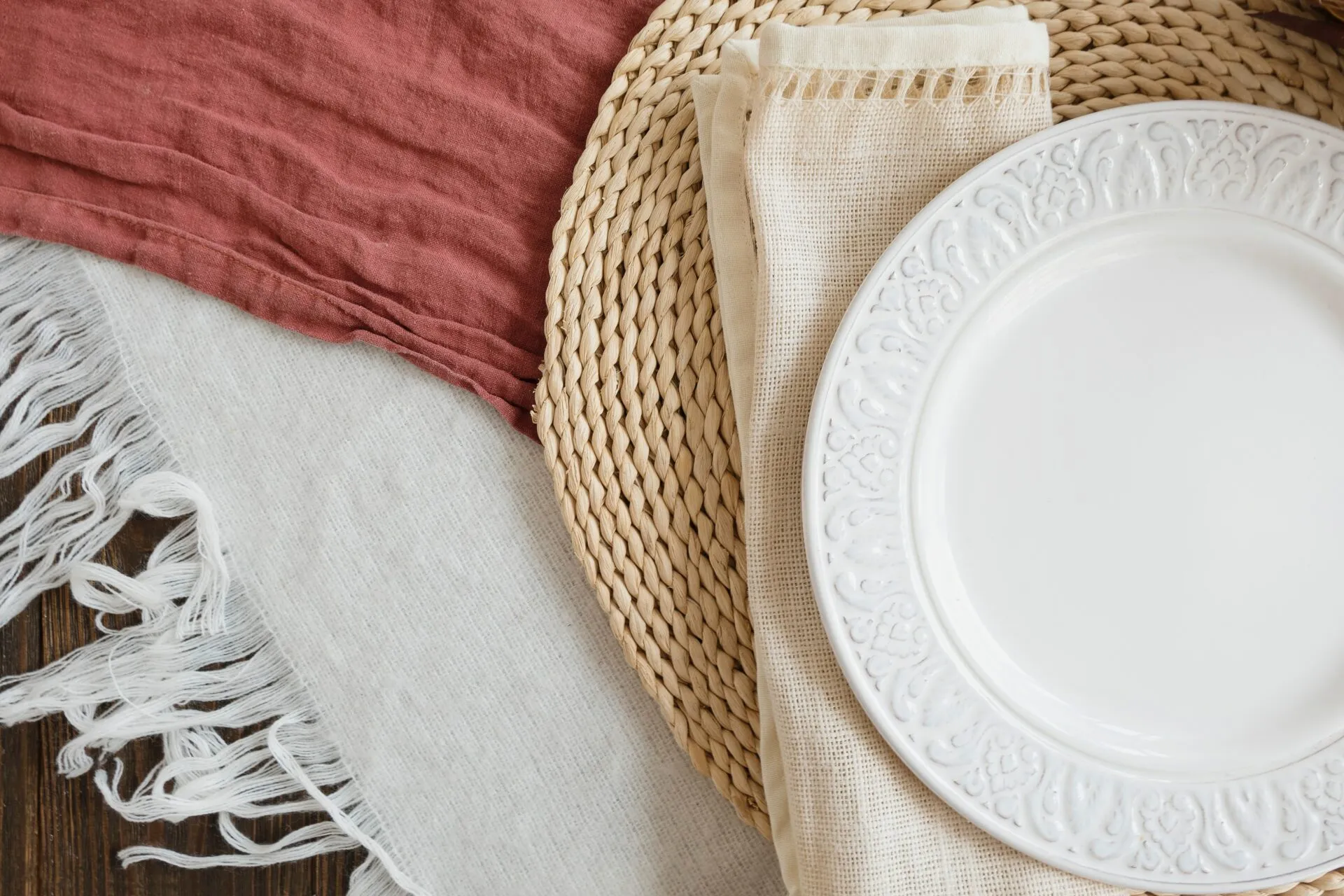 Gedeckter Tisch mit rostroter Leinenserviette, geflochtenem Untersetzer und weißem Teller